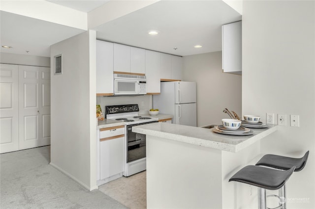 kitchen featuring white cabinetry, a kitchen breakfast bar, kitchen peninsula, white appliances, and light carpet