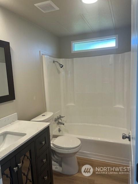 full bath with visible vents, toilet, vanity, shower / tub combination, and wood finished floors