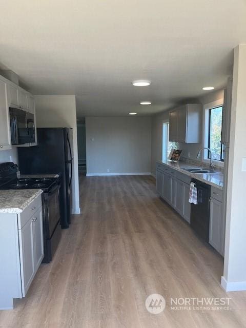 kitchen with baseboards, black appliances, a sink, and light wood-style floors