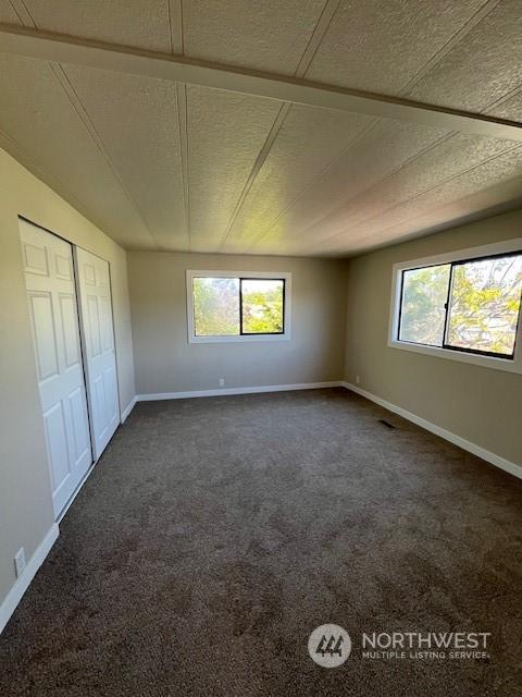 unfurnished bedroom with multiple windows, dark carpet, and baseboards