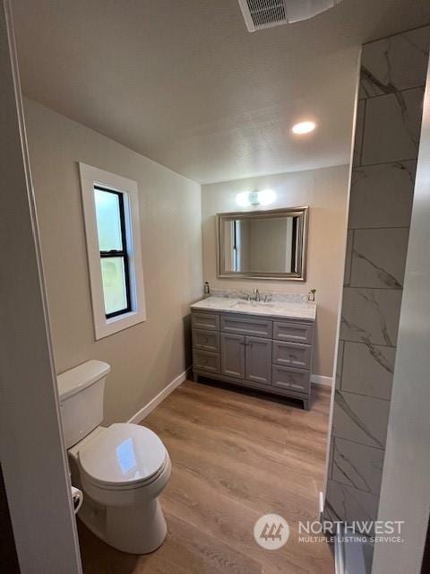 bathroom with toilet, wood finished floors, visible vents, and baseboards