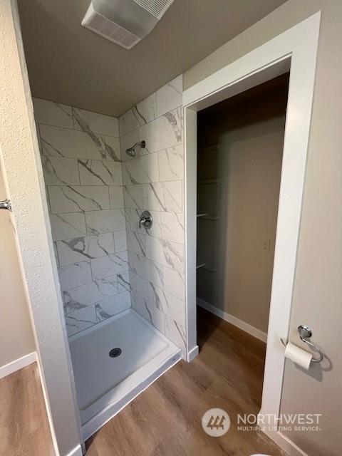 full bathroom with a tile shower, wood finished floors, visible vents, and baseboards