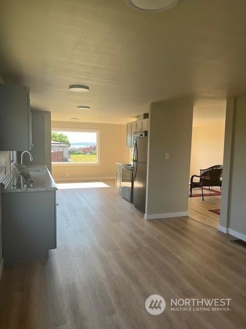 kitchen with range with electric cooktop, wood finished floors, a sink, baseboards, and freestanding refrigerator