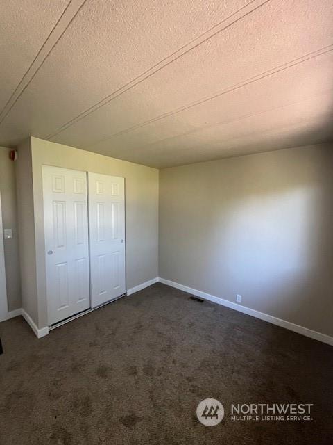 unfurnished bedroom featuring dark colored carpet, visible vents, a textured ceiling, and baseboards