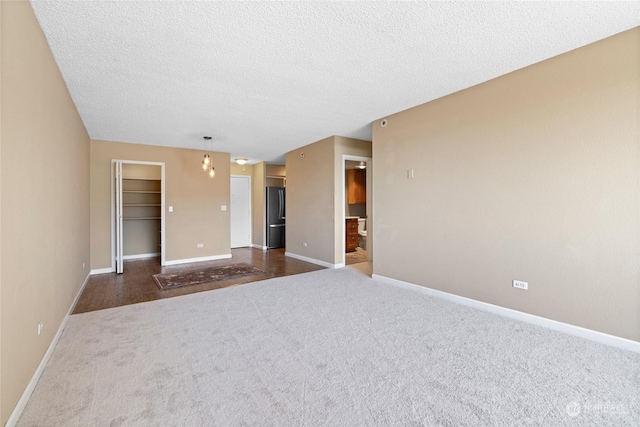 unfurnished room with dark carpet, a textured ceiling, and baseboards