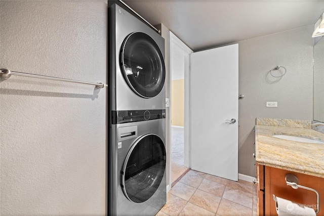 washroom featuring light tile patterned floors, laundry area, a textured wall, stacked washer and clothes dryer, and a sink