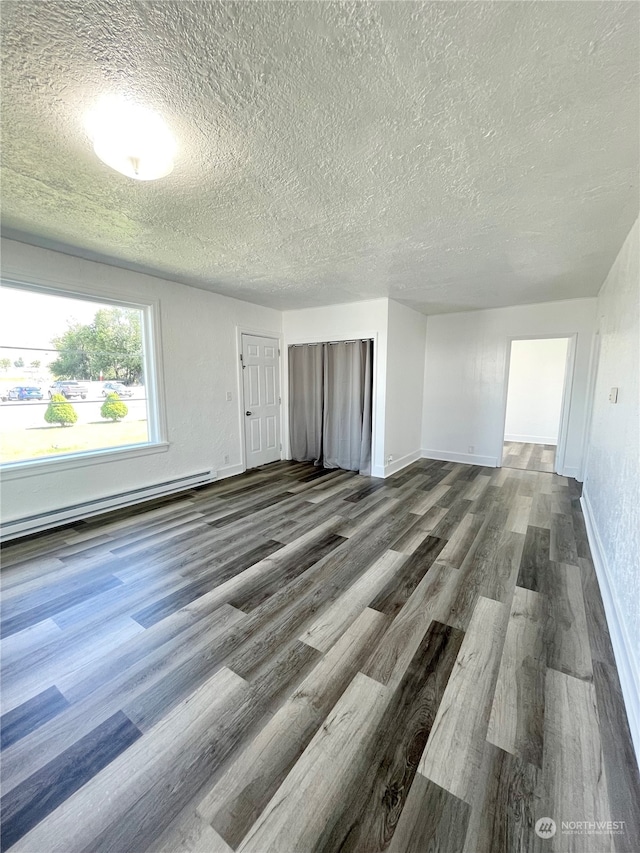 unfurnished living room featuring a baseboard heating unit, a textured ceiling, and dark hardwood / wood-style floors