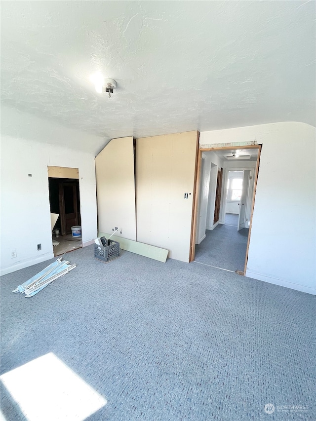 empty room featuring a textured ceiling, carpet flooring, and vaulted ceiling