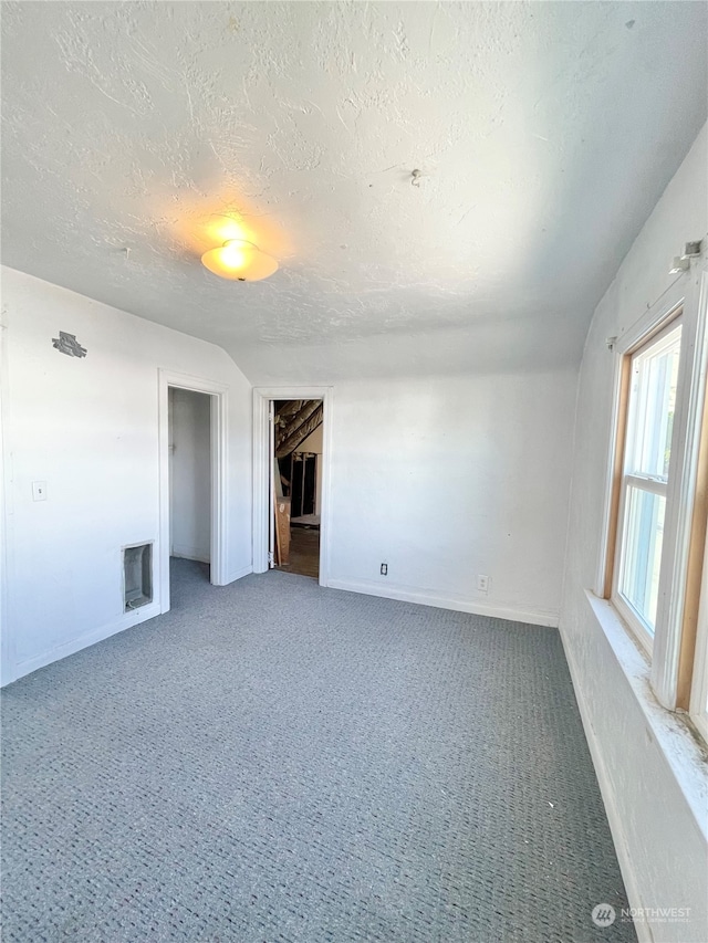 interior space with a textured ceiling, carpet floors, and vaulted ceiling