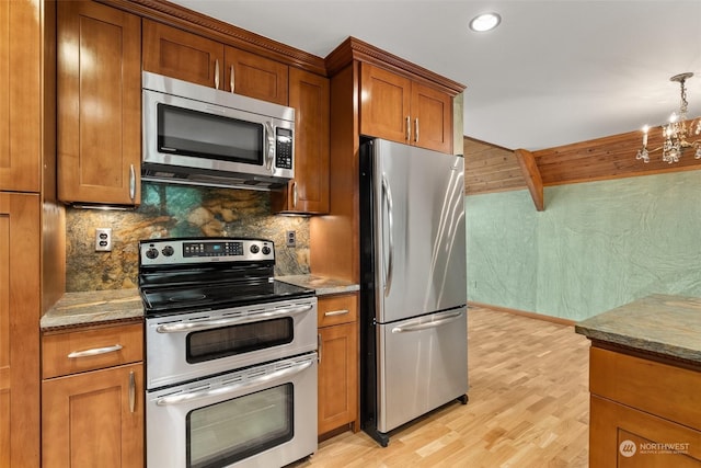 kitchen featuring tasteful backsplash, light stone counters, a chandelier, appliances with stainless steel finishes, and light wood-type flooring