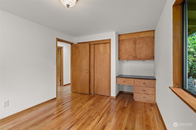 unfurnished bedroom with light hardwood / wood-style flooring, built in desk, and a closet