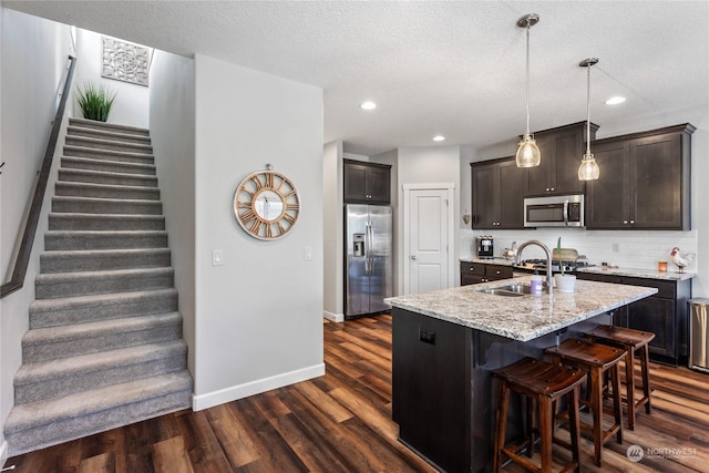 kitchen featuring dark brown cabinetry, appliances with stainless steel finishes, dark hardwood / wood-style flooring, an island with sink, and backsplash