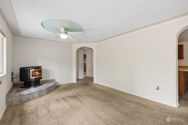 unfurnished living room featuring carpet, ceiling fan, and a wood stove