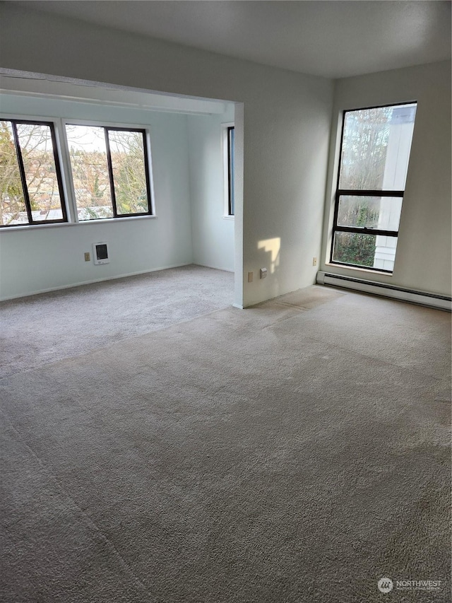 carpeted empty room featuring a baseboard heating unit