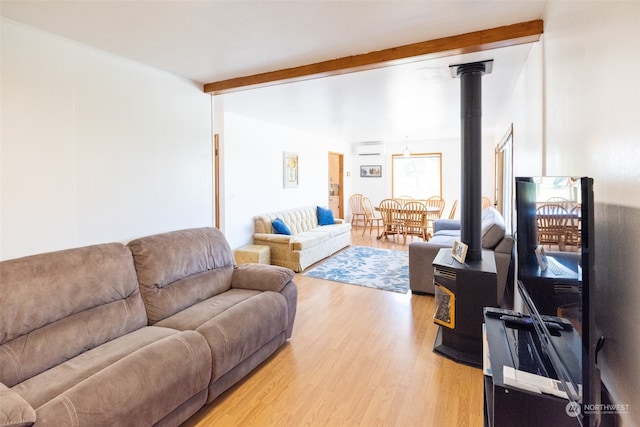 living room featuring a wall mounted AC, a wood stove, beam ceiling, and hardwood / wood-style flooring