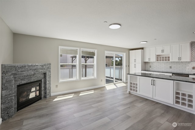 kitchen with a fireplace, white cabinetry, light wood-type flooring, and tasteful backsplash