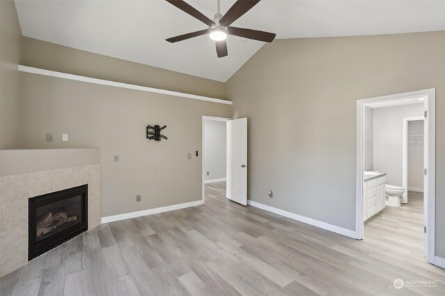 unfurnished living room featuring high vaulted ceiling, a tiled fireplace, ceiling fan, and light wood-type flooring