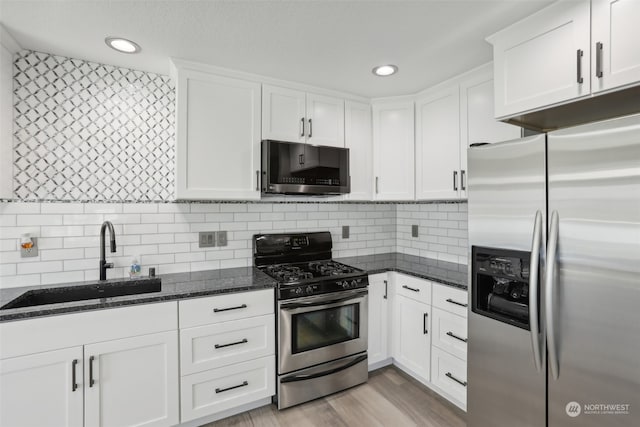 kitchen featuring white cabinetry, stainless steel appliances, sink, dark stone countertops, and light hardwood / wood-style flooring