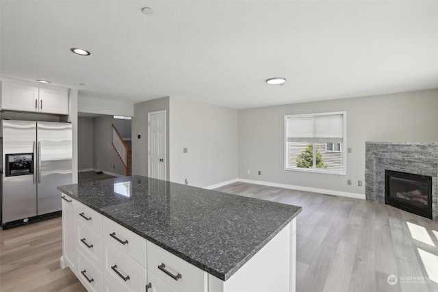 kitchen featuring a fireplace, white cabinets, a kitchen island, stainless steel fridge, and light hardwood / wood-style flooring