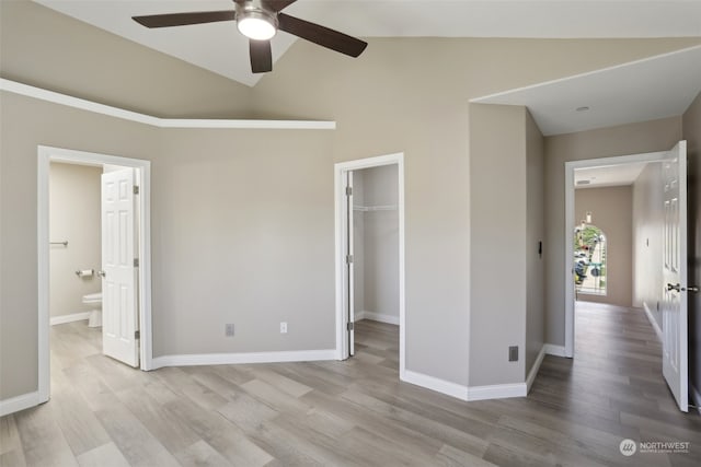 unfurnished bedroom featuring ceiling fan, a walk in closet, wood-type flooring, vaulted ceiling, and ensuite bath