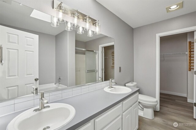 bathroom with a skylight, toilet, wood-type flooring, and double vanity