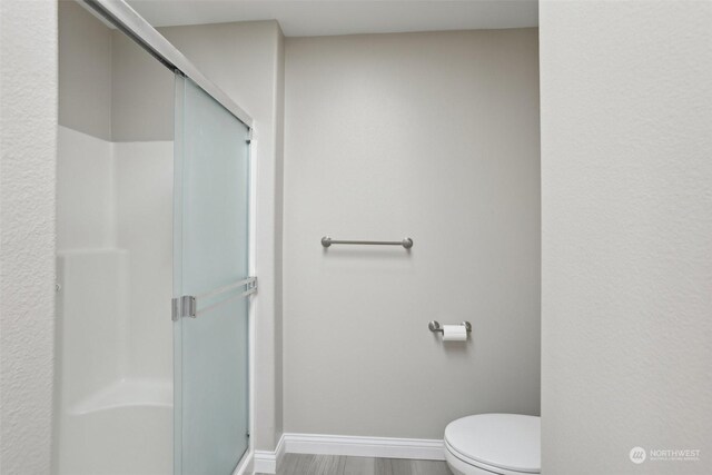 bathroom featuring a shower with shower door and toilet