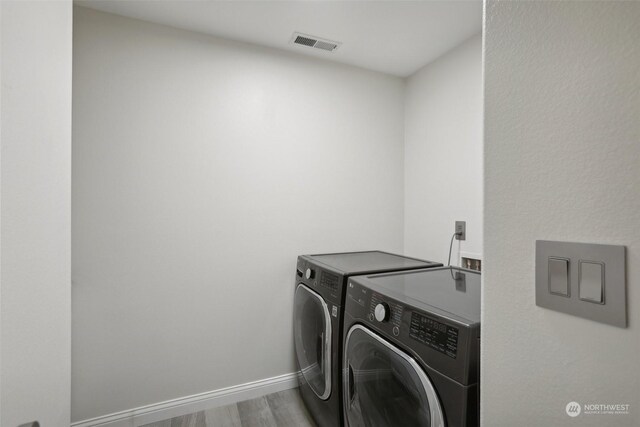 clothes washing area with washing machine and dryer and hardwood / wood-style flooring