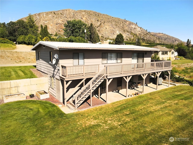 rear view of property featuring a yard, a deck with mountain view, and a patio area