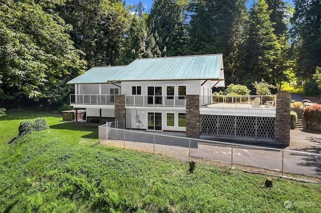 back of house with metal roof, a balcony, fence, a lawn, and stucco siding