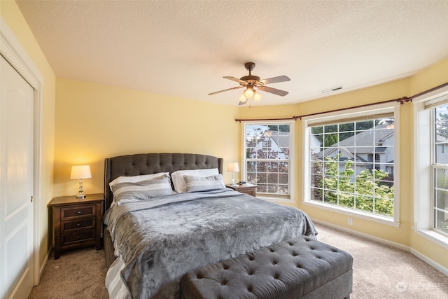 carpeted bedroom featuring ceiling fan, a closet, a textured ceiling, and multiple windows