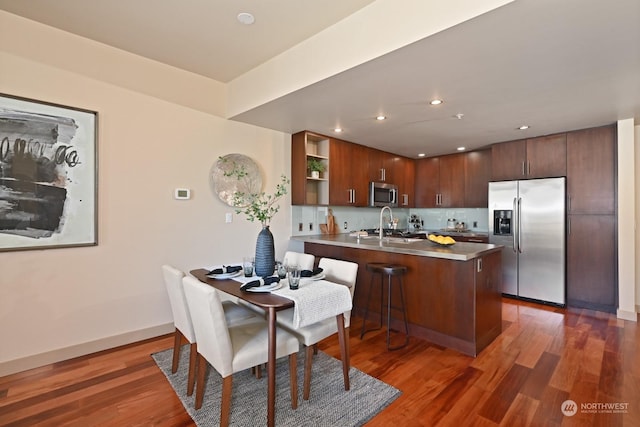 kitchen featuring a kitchen breakfast bar, tasteful backsplash, dark hardwood / wood-style floors, kitchen peninsula, and appliances with stainless steel finishes