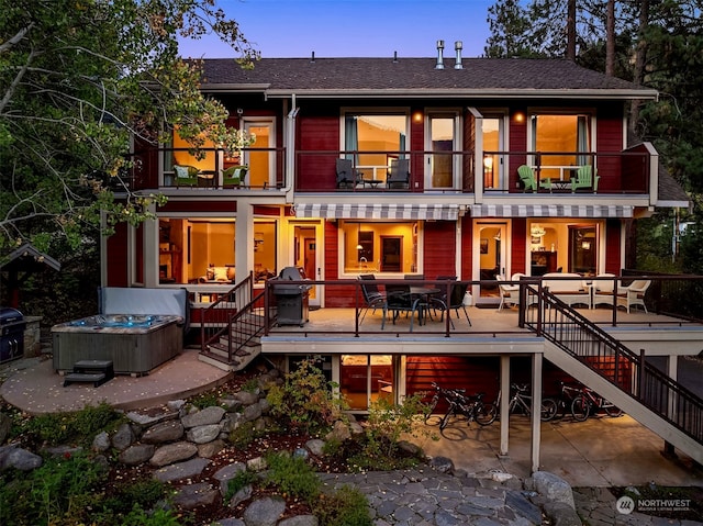 back house at dusk featuring a balcony and a patio area