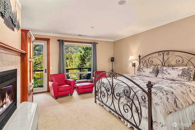 carpeted bedroom with ornamental molding, a tiled fireplace, and access to exterior