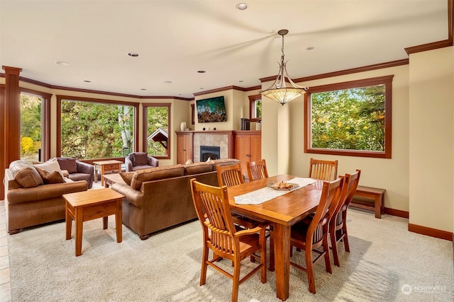 dining space with ornamental molding, a tile fireplace, and light carpet