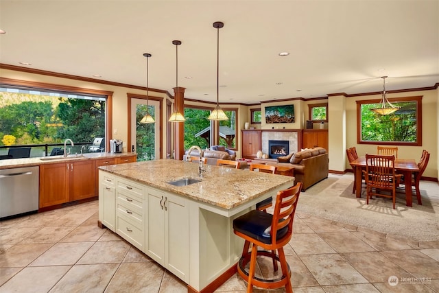 kitchen with an island with sink, dishwasher, a tiled fireplace, light stone countertops, and sink