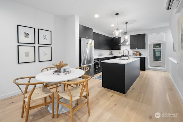 kitchen with a center island with sink, an AC wall unit, decorative light fixtures, light hardwood / wood-style floors, and stainless steel refrigerator