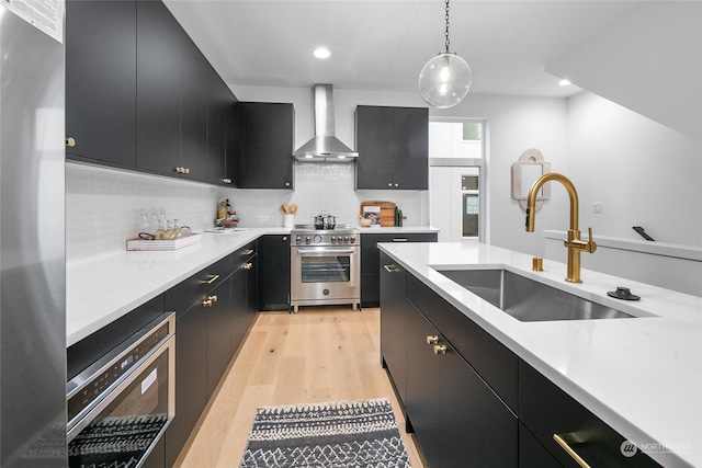 kitchen featuring sink, wall chimney exhaust hood, pendant lighting, appliances with stainless steel finishes, and light wood-type flooring