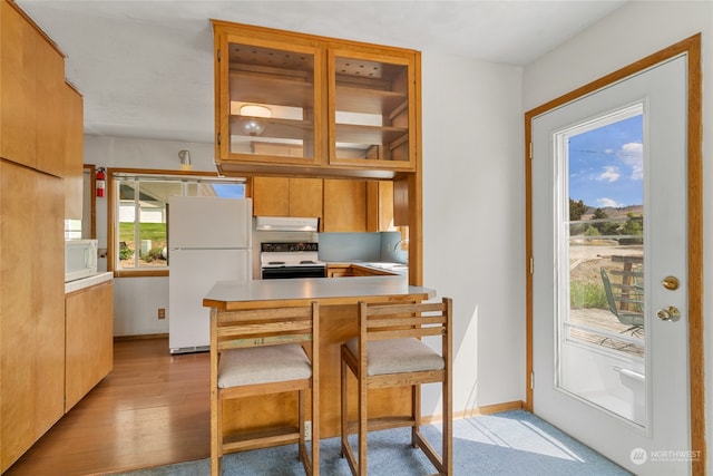 kitchen featuring light hardwood / wood-style floors, kitchen peninsula, white appliances, sink, and a kitchen bar