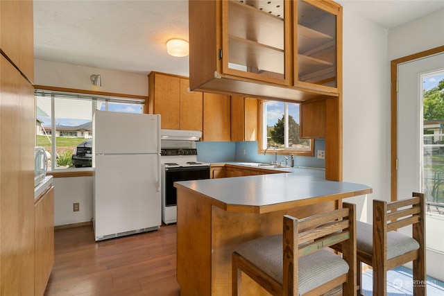 kitchen featuring light hardwood / wood-style floors, kitchen peninsula, white appliances, sink, and a breakfast bar area