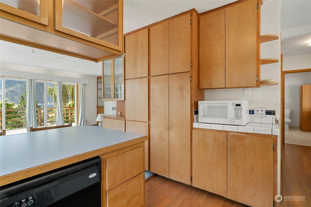 kitchen with black dishwasher, light wood-type flooring, and tile countertops