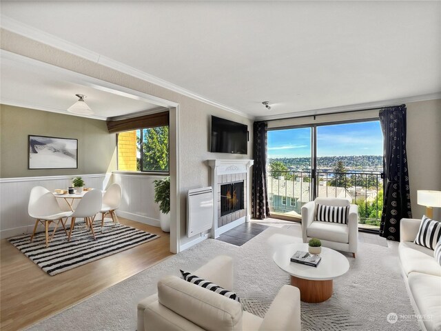 living room featuring a tiled fireplace, a healthy amount of sunlight, hardwood / wood-style flooring, and ornamental molding