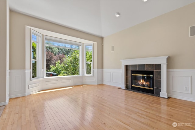 3377 Topaz Ct, Bellingham, WA 98226 - unfurnished living room featuring light wood-style flooring, wainscoting, a decorative wall, a tiled fireplace, and a towering ceiling