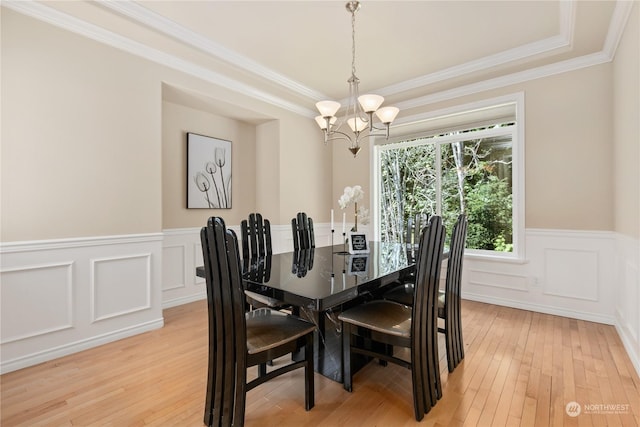 dining room featuring ornamental molding, light wood-type flooring, a raised ceiling, and a notable chandelier