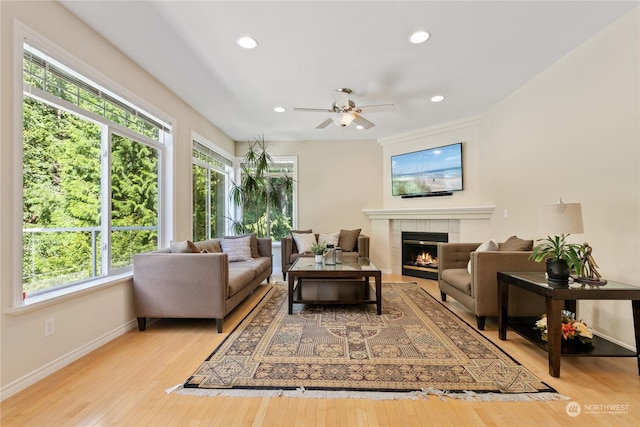 living room with ceiling fan, a healthy amount of sunlight, light wood-type flooring, and a tile fireplace