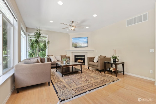 living room featuring a tile fireplace, ceiling fan, and light hardwood / wood-style flooring