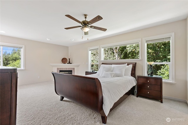 bedroom with ceiling fan, light carpet, and a tile fireplace