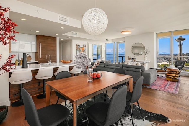 dining room featuring light wood-type flooring, a water view, a wall of windows, and sink