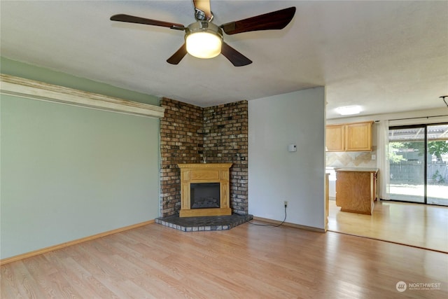 unfurnished living room featuring a large fireplace, light hardwood / wood-style flooring, and ceiling fan