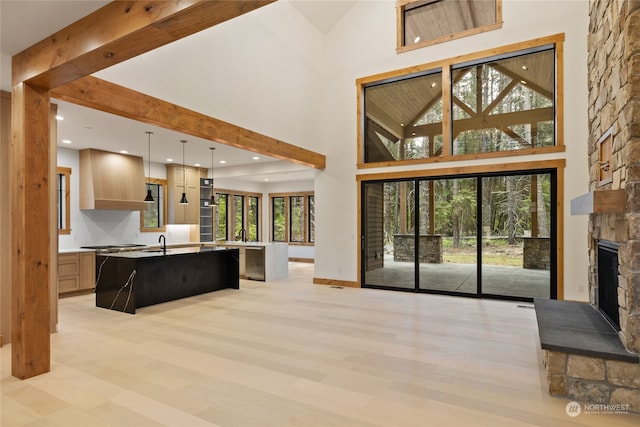 kitchen featuring a kitchen breakfast bar, pendant lighting, light brown cabinets, a stone fireplace, and an island with sink