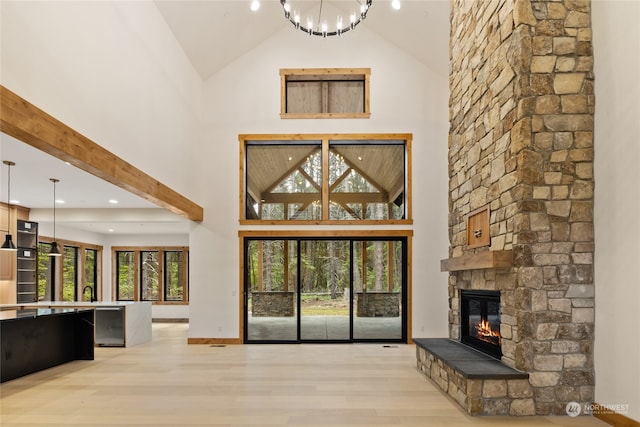 unfurnished living room with a notable chandelier, light wood-type flooring, a fireplace, and high vaulted ceiling